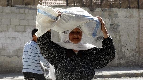 A woman carries a sack of food aid on her head in Ghouta, an eastern suburb of Damascus