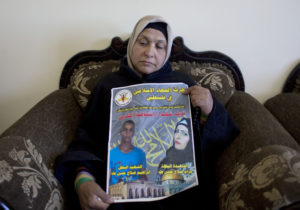 Fatema Taha, 40, the mother of Maram, 24 and Ibrahim Taha, 16, displays a poster with their pictures and Arabic that reads, "Islamic Jihad in Palestine celebrates the martyrs of Jerusalem's uprising," at the family house, in the West Bank village of Qatana, near Ramallah.